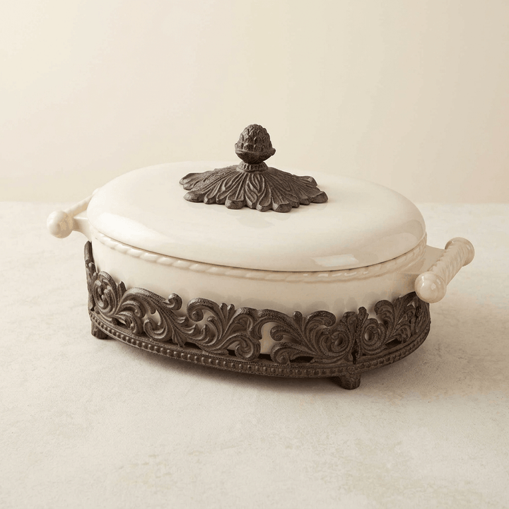 Closer view of Bellavita cream stoneware casserole showing scrolling dark metal base and leaf lid finial