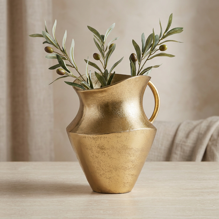 Gold cast aluminum decorative pitcher styled with faux olive branches on a light stone tabletop.