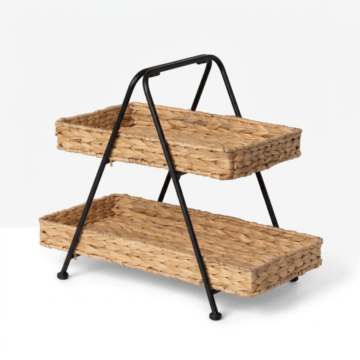 Seraphine Two-Tier Basket Stand shown at a three-quarter angle on a soft white background, two woven hyacinth baskets on a black iron stand with arched handle
