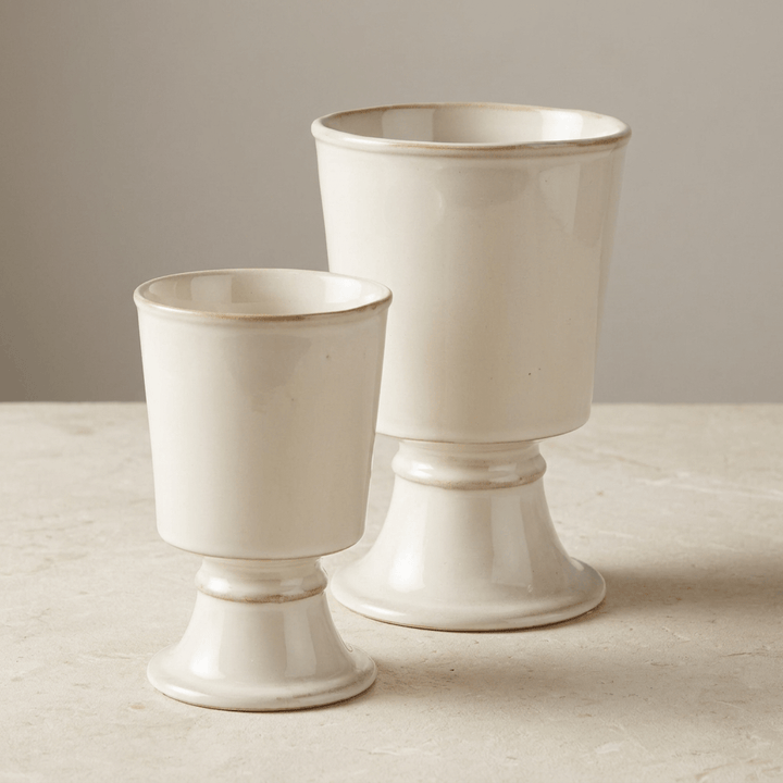 Two cream stoneware footed cachepots in complementary sizes on a pale studio surface.