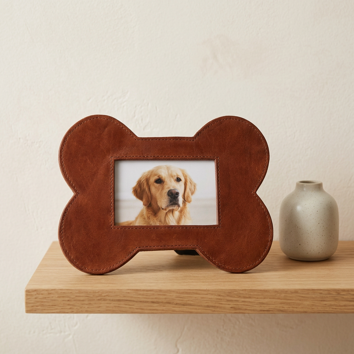 Brown leather bone-shaped pet photo frame styled on an oak shelf beside a neutral ceramic vase.
