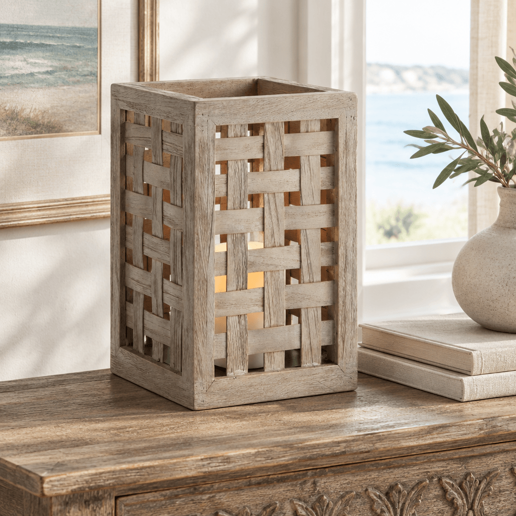 Gray woven teak hurricane with a flameless LED candle on an indoor console beside books and ceramics.