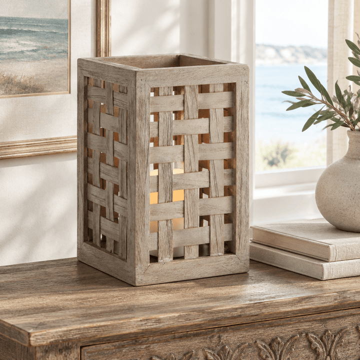 Gray woven teak hurricane with a flameless LED candle on an indoor console beside books and ceramics.