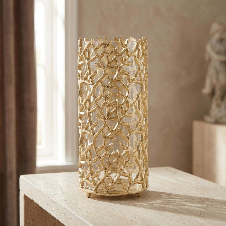 Gold vine hurricane candle holder with clear glass insert styled on a pale stone console.