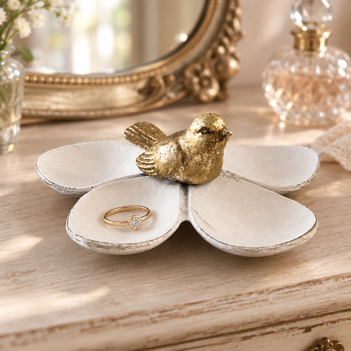 Flower jewelry dish with gold bird and a ring on a pale wood vanity