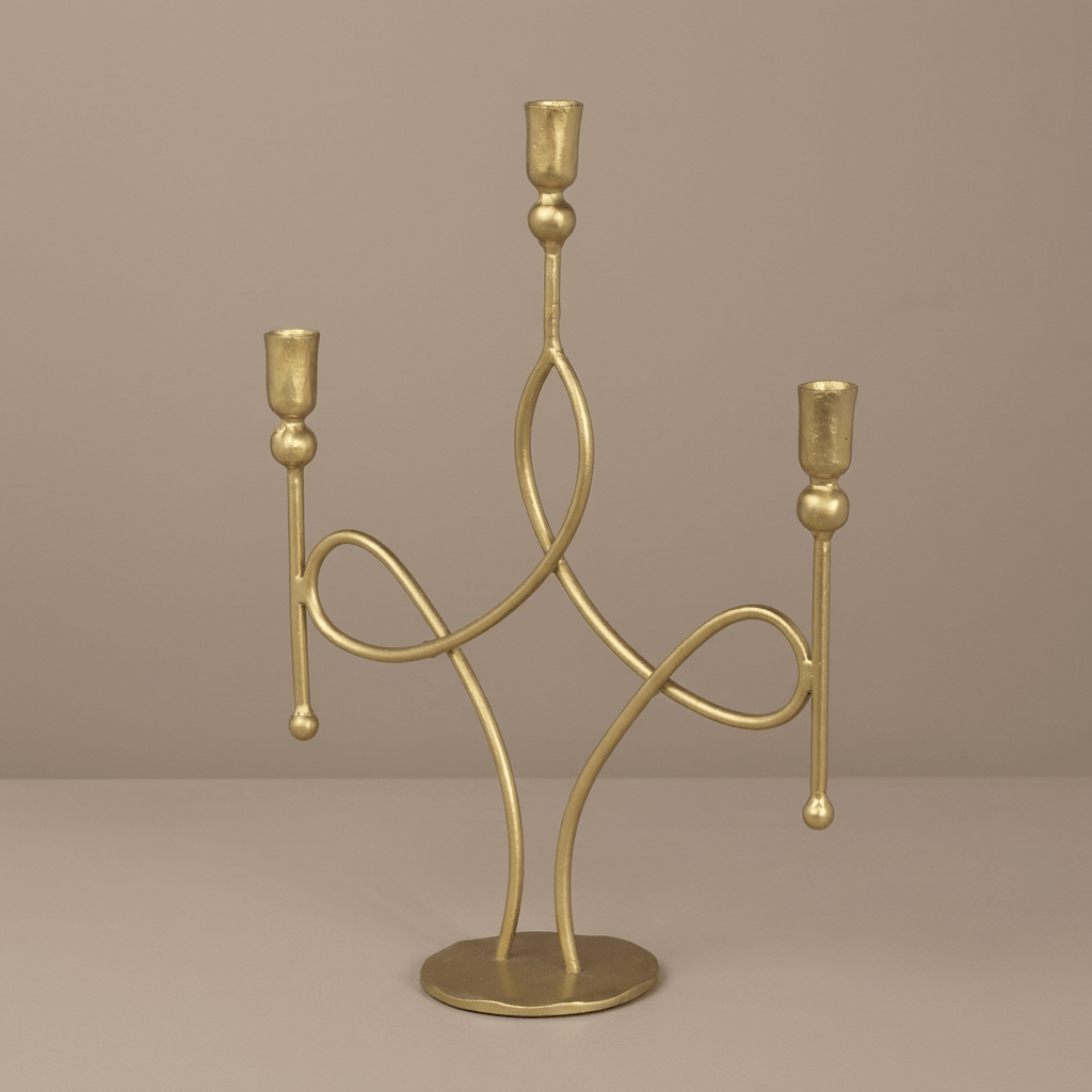 Three-arm antique gold candelabra with looping iron scrolls and a round base against a taupe studio background.