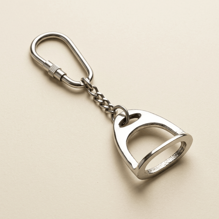 Polished silver-tone English stirrup keychain with short link chain and screw-lock ring on an ivory background.