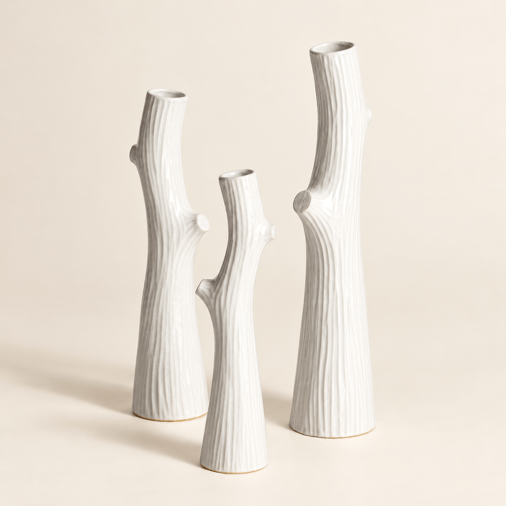 Three white ceramic vases showing slender branch silhouettes, narrow openings, and faux-bois texture.