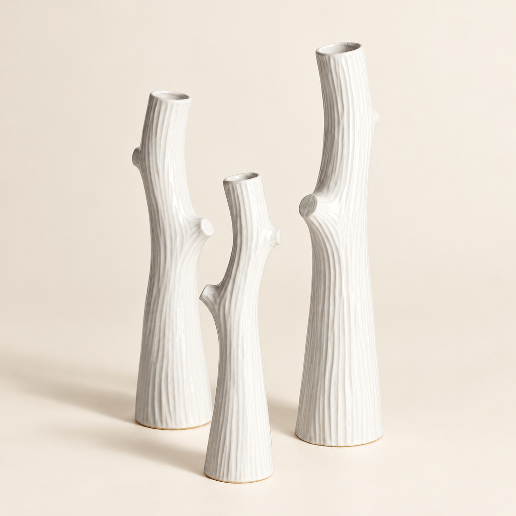 Three white ceramic vases showing slender branch silhouettes, narrow openings, and faux-bois texture.