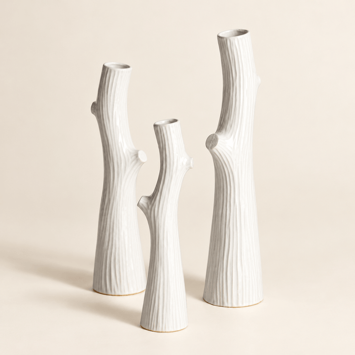 Three white ceramic vases showing slender branch silhouettes, narrow openings, and faux-bois texture.