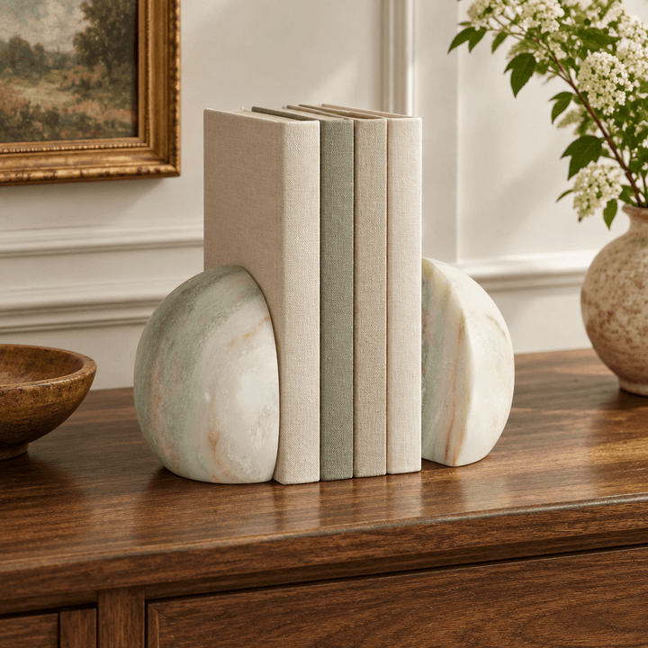 Rounded green and white marble bookends holding linen-bound books on a walnut foyer console.