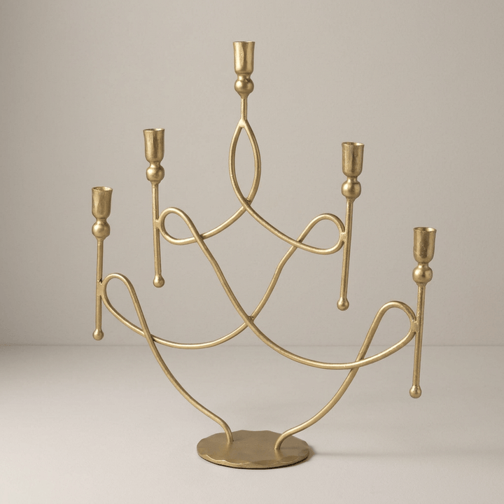 Five-arm antique gold iron candelabra with staggered candle cups against a warm gray studio background.
