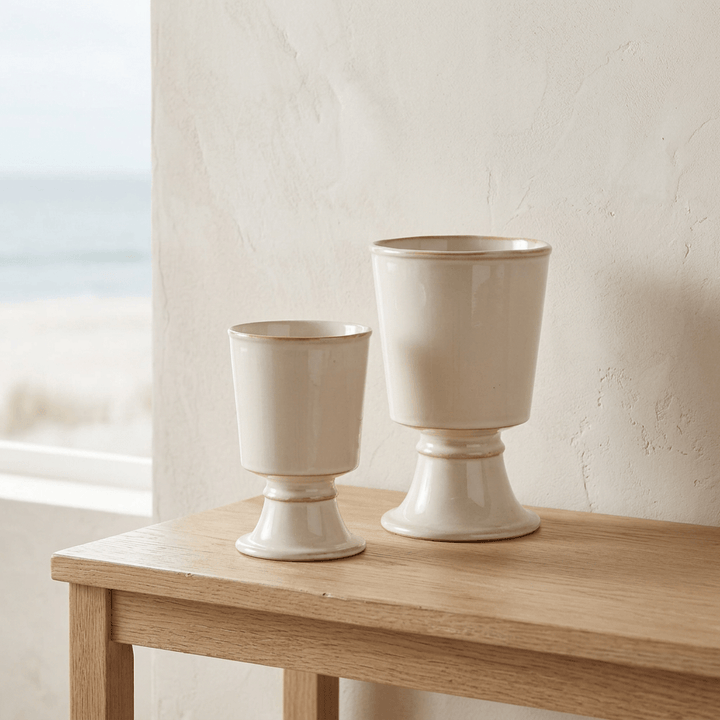 Pair of cream stoneware pedestal cachepots styled on a light oak console in a neutral coastal interior.