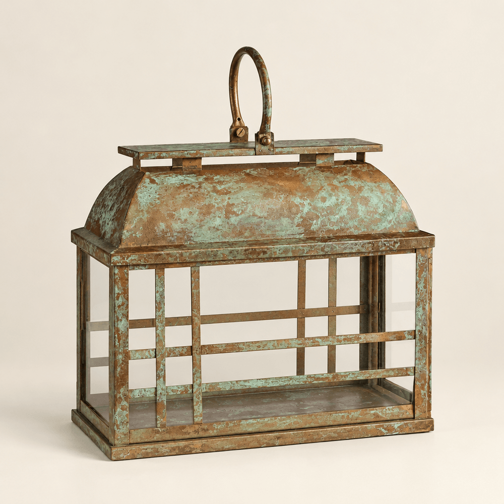 Empty weathered iron and glass lantern showing its curved roof, oval handle, and gold-and-green patina.