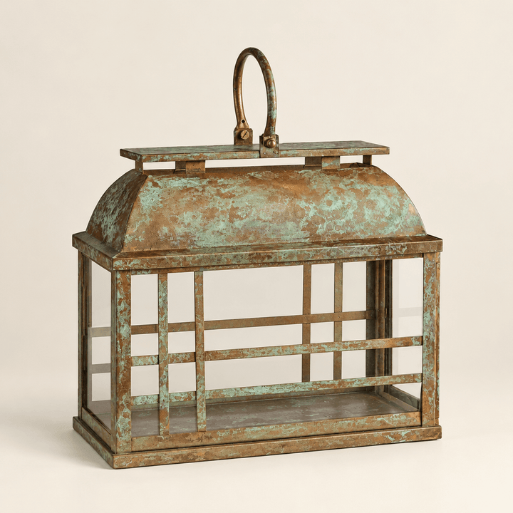 Empty weathered iron and glass lantern showing its curved roof, oval handle, and gold-and-green patina.