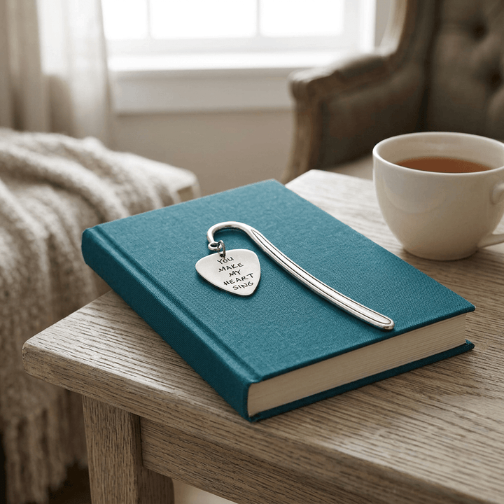 Silver-tone guitar-pick charm bookmark styled with a clothbound book and tea cup in a reading nook.