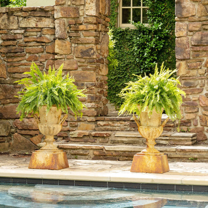 Large Rustic Metal Garden Urn with Aged Patina Finish near stone wall with lush greenery