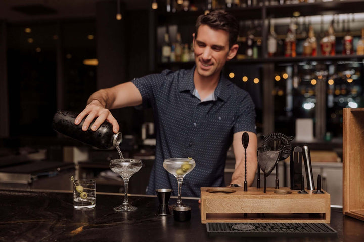 Mixologist using Vintage-Style Bartender Kit with Mango Wood Case & Bar Tools in a modern bar setting.
