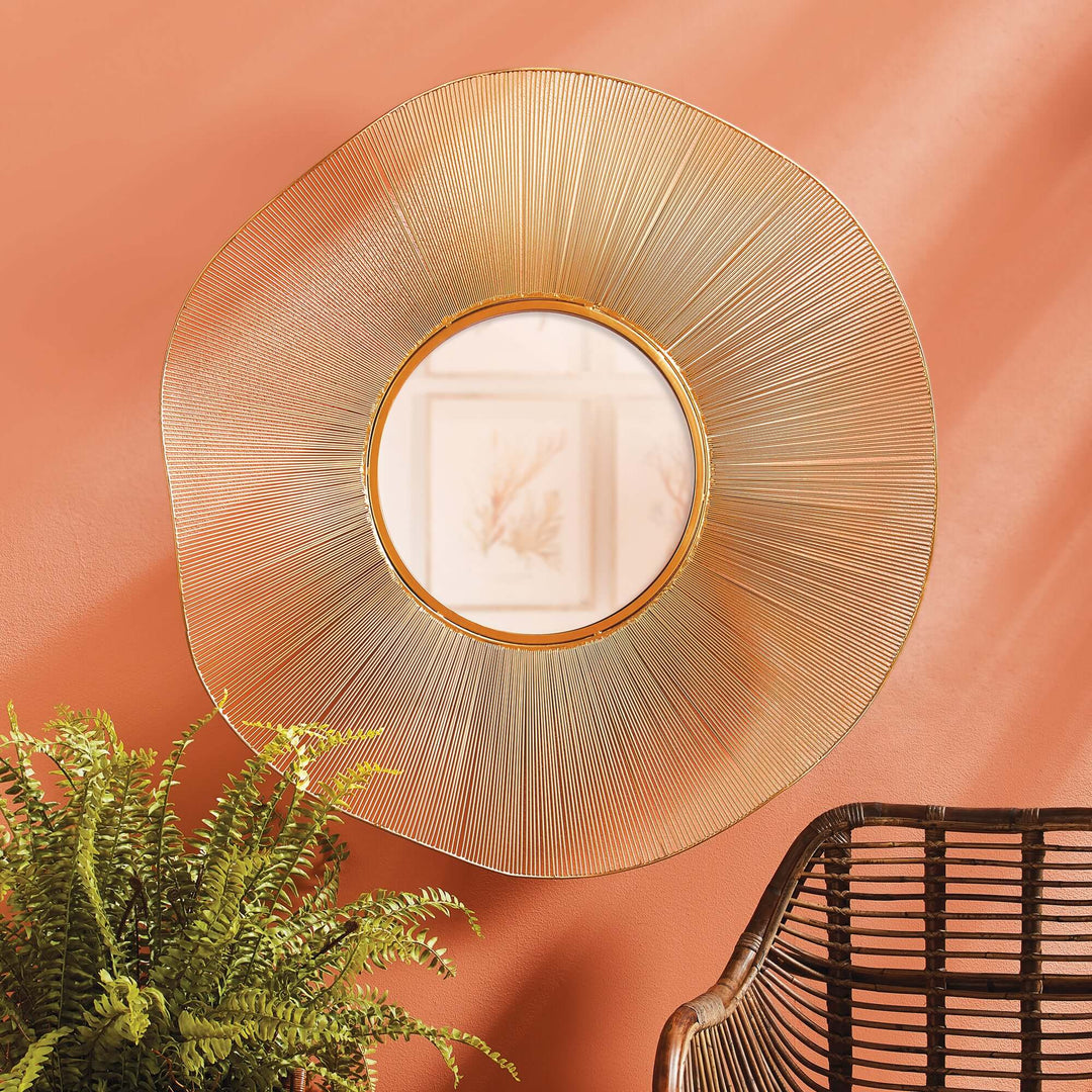 Mid-century sunburst wall mirror with gold wire frame against an orange wall, showcasing elegant design.