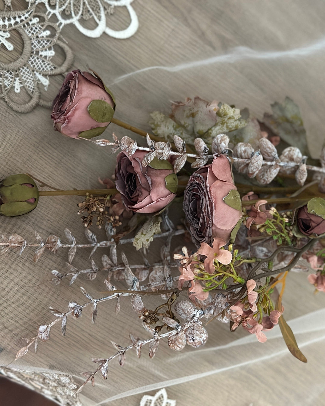 Purple faux flower bouquet laid on lace to show its branching composition