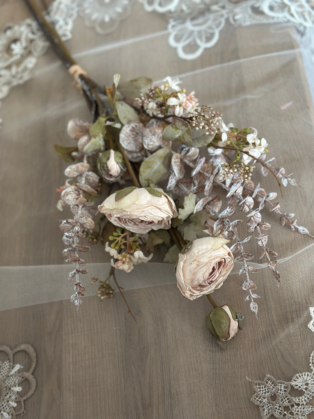 White faux flower bouquet laid on lace with cream blooms and pale foliage