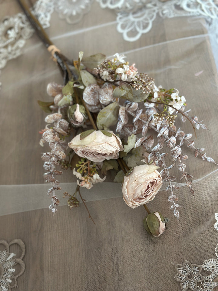 White faux flower bouquet laid on lace with cream blooms and pale foliage