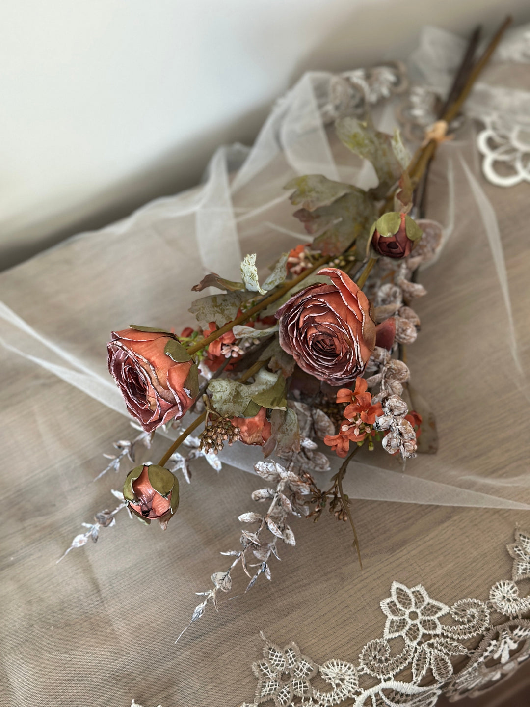 Orange faux flower bouquet laid on lace with rust-toned blooms