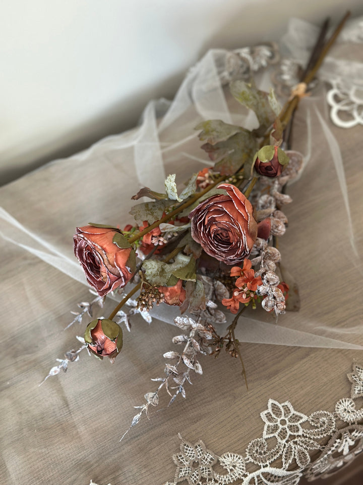 Orange faux flower bouquet laid on lace with rust-toned blooms