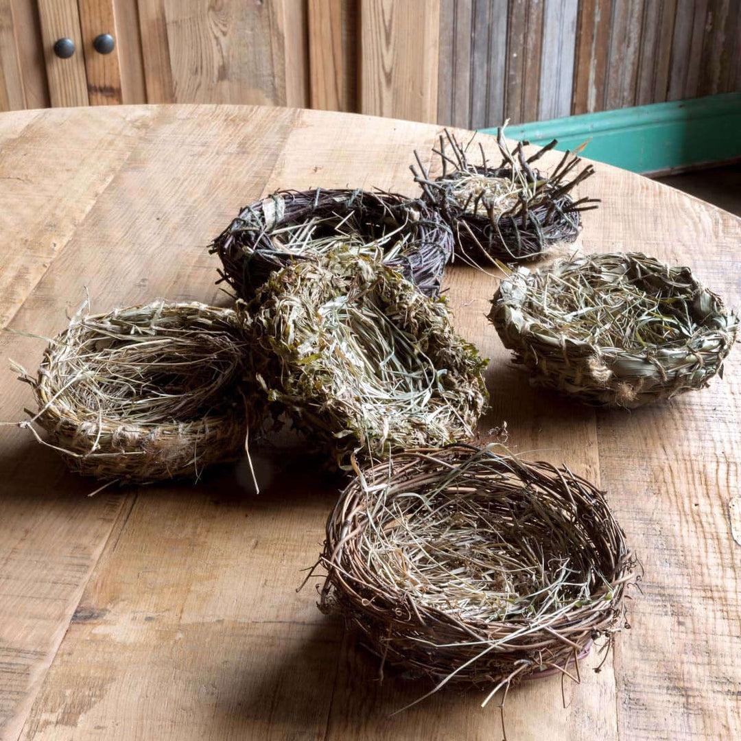 Handcrafted rattan, grass, and bamboo bird nests displayed on a wooden table, showcasing unique textures and rustic charm.