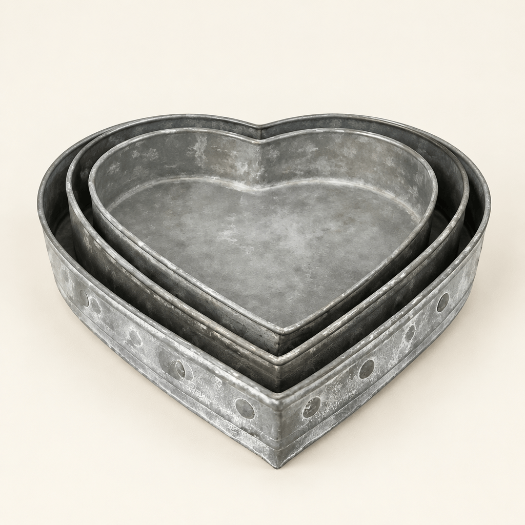 Three nested heart-shaped metal trays with a weathered silver-tone finish on an ivory background