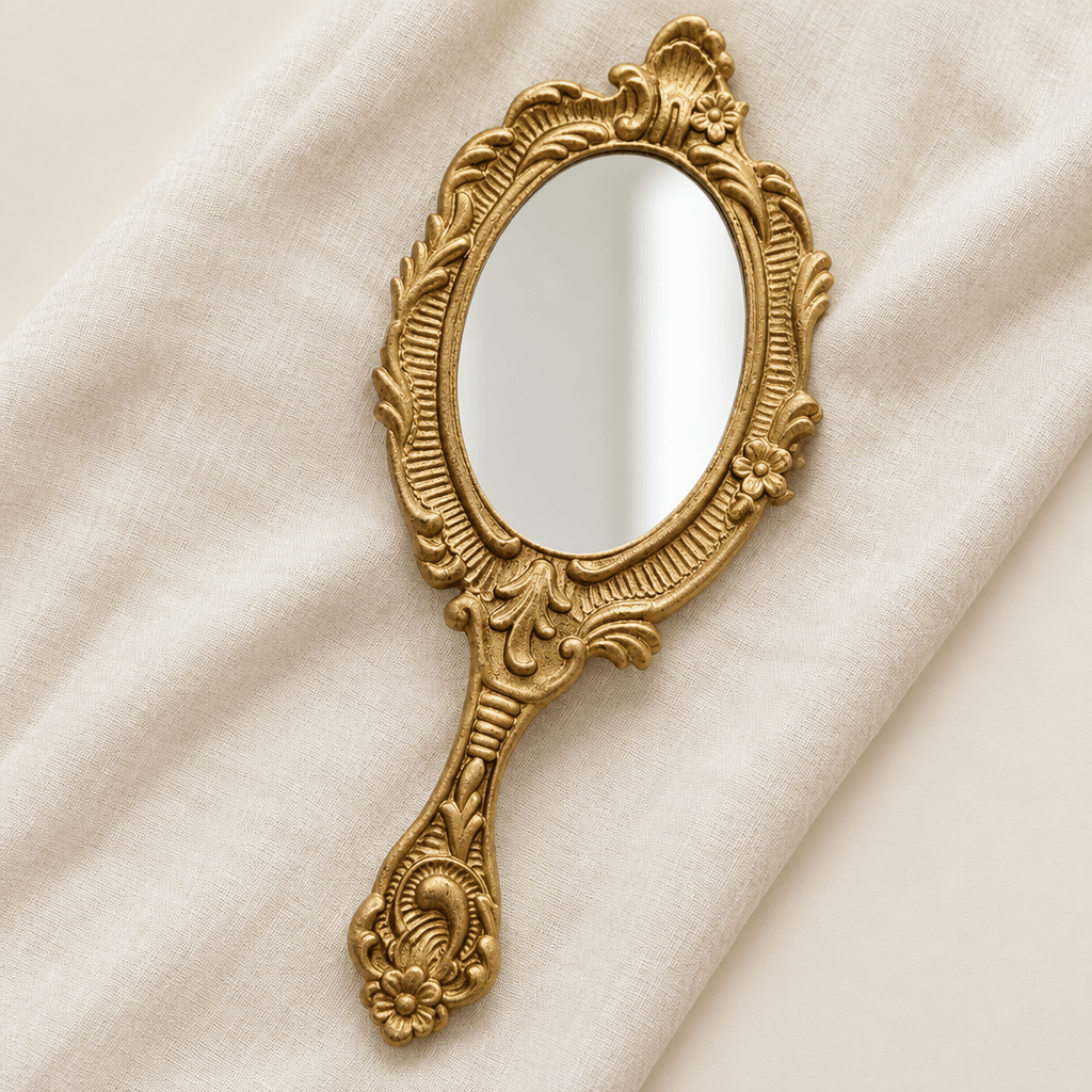 Ornate gold-tone oval handheld mirror styled on ivory linen in a studio setting