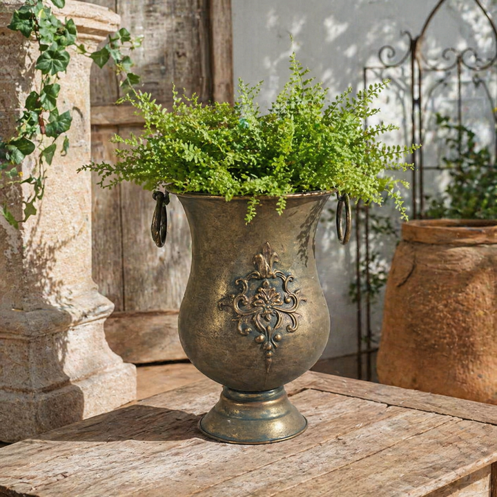 Ornate Iron Urn Planter with Ring Handles filled with greenery on a rustic table