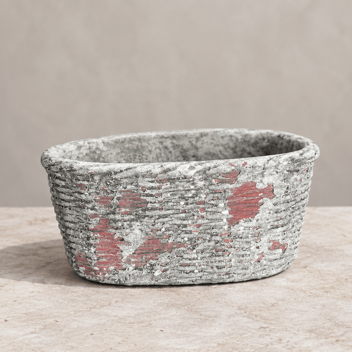 Oval concrete planter on pale stone showing raised basket texture and weathered reddish accents.