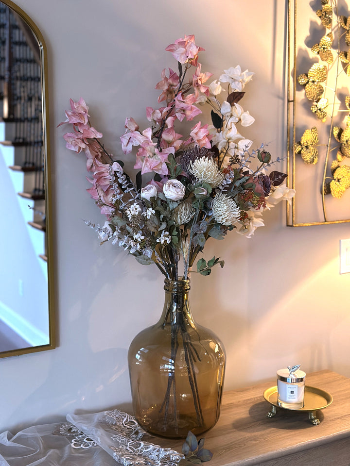 Pink and white bougainvillea stems mixed with flowers in an amber glass vase