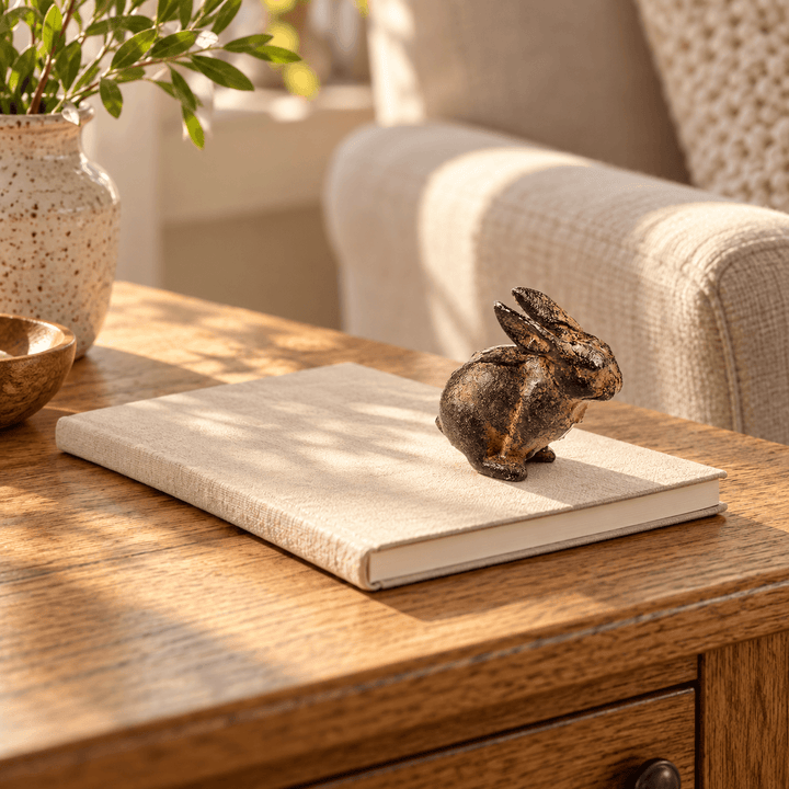 Small cast iron rabbit on a closed notebook beside a linen armchair