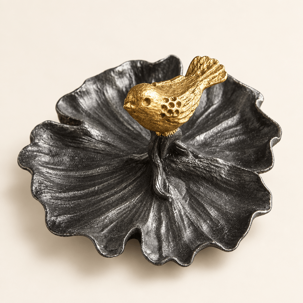 Dark pewter leaf-shaped jewelry tray with a gold bird on an ivory studio backdrop.