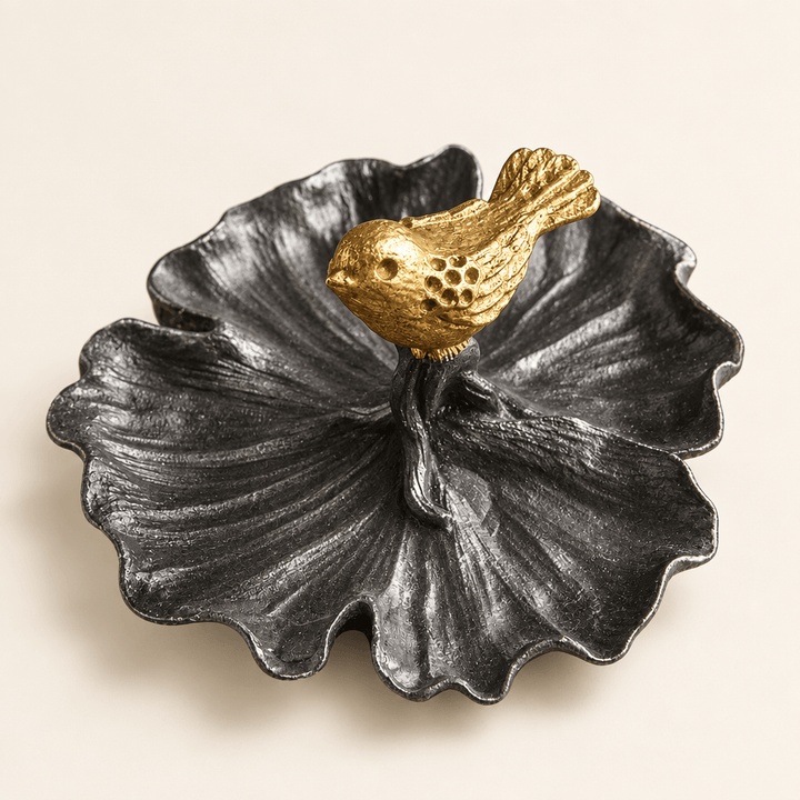 Dark pewter leaf-shaped jewelry tray with a gold bird on an ivory studio backdrop.