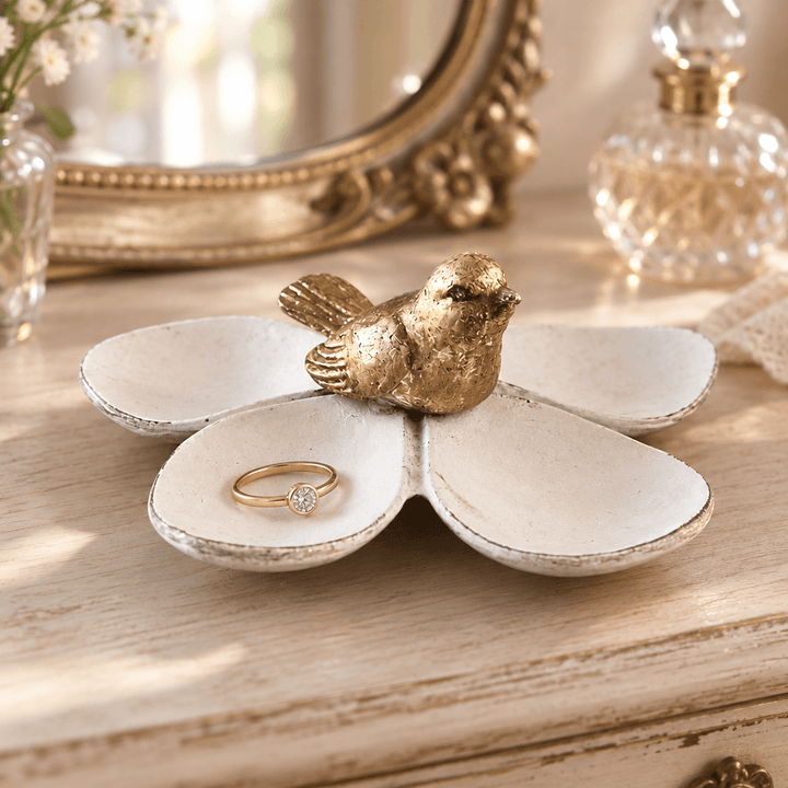 Flower jewelry dish with gold bird and a ring on a pale wood vanity