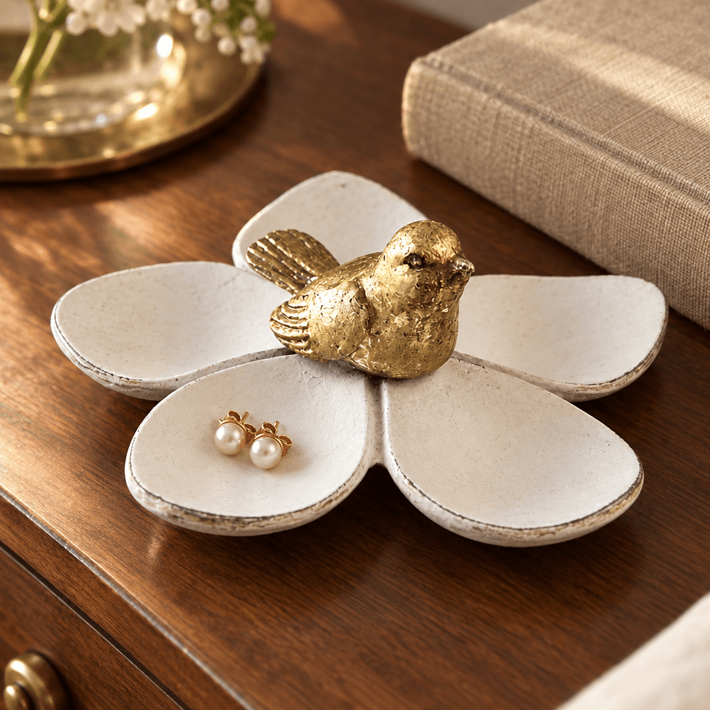 White flower jewelry dish with gold bird and stud earrings on a walnut bedside table