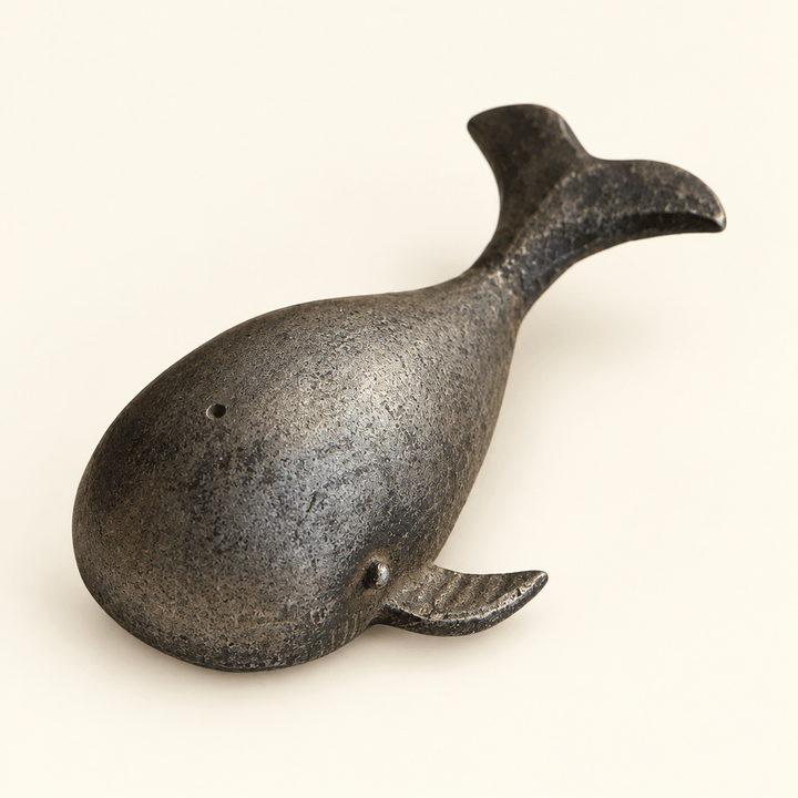 Grey-black pewter whale bottle opener on an ivory studio backdrop.