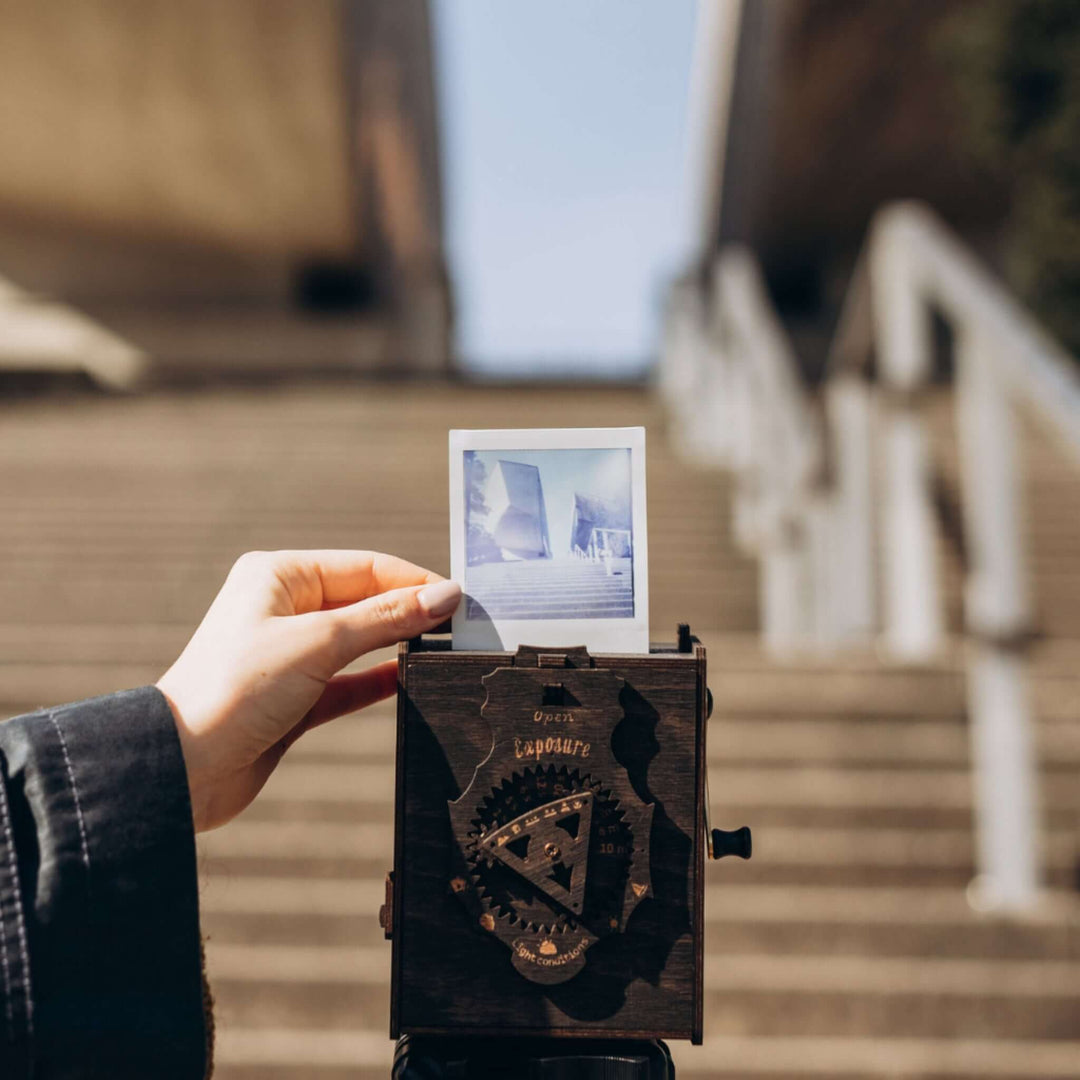 Hands holding Pinhole Square Instant Film Camera DIY Kit capturing a vintage-inspired instant photo on stairs.