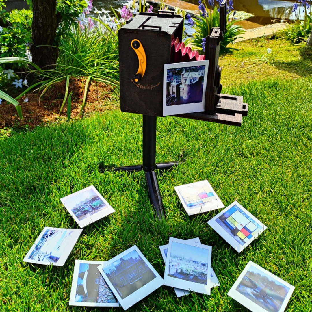 Pinhole Square Instant Film Camera DIY Kit displayed outdoors with developed photos scattered on the grass
