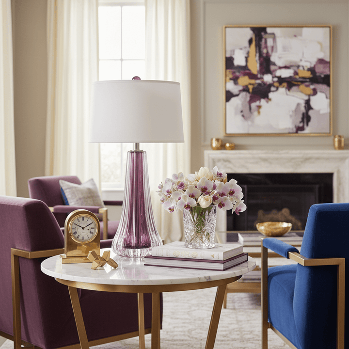 Living room with a round table, chairs, and decorative items. A glass table lamp is on a table.