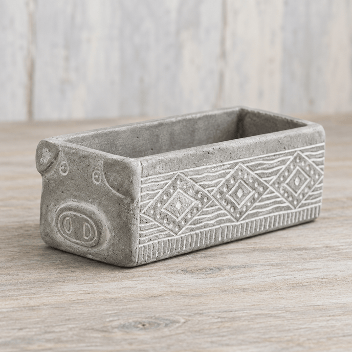 Gray cement pig planter showing its raised snout, small ears, and etched geometric side pattern