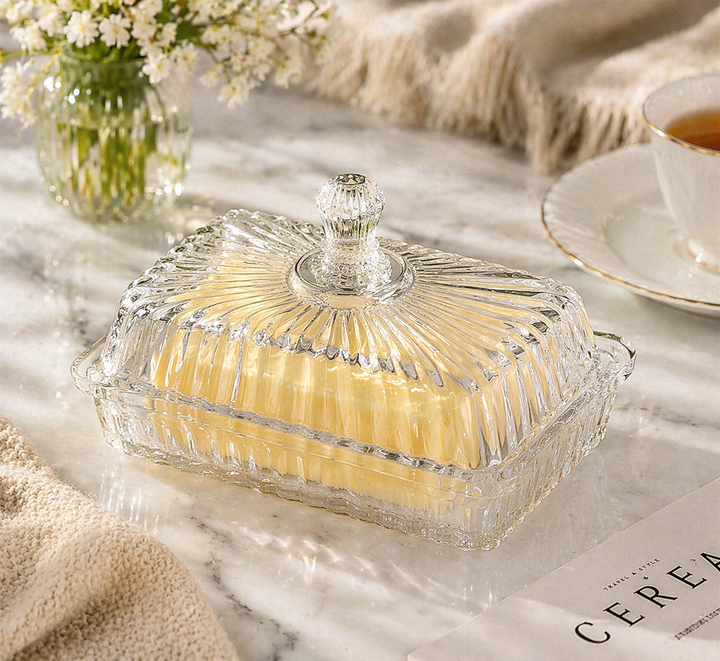 Ribbed glass butter dish with lid holding butter on marble