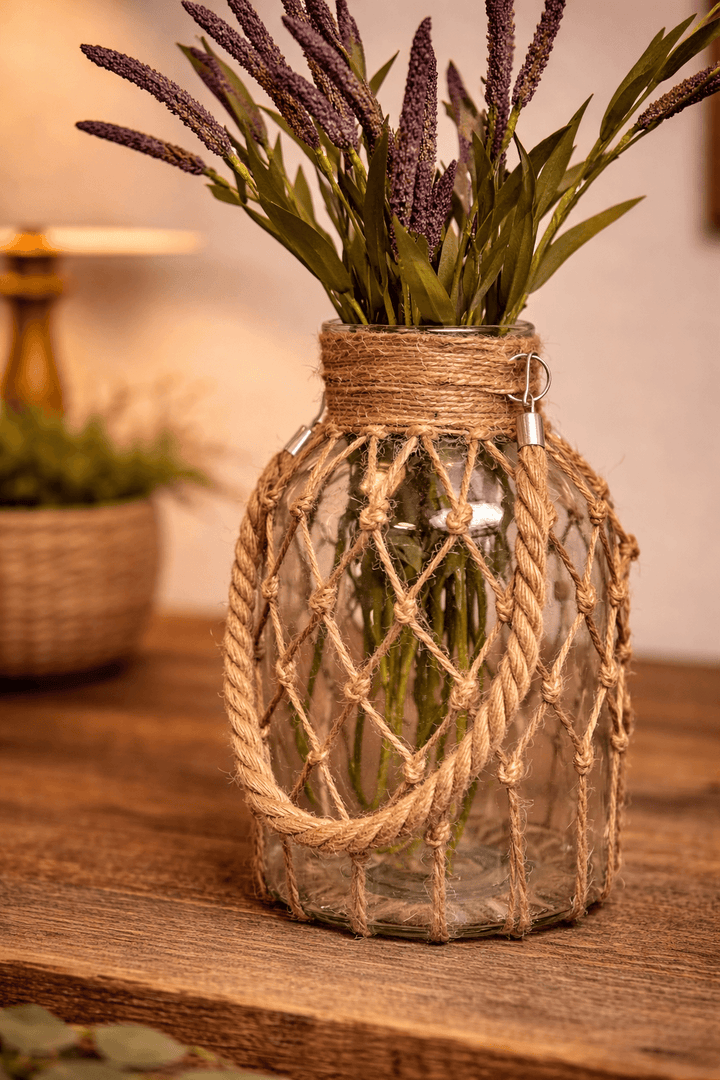 Rope-net bottle vase holding purple stems on a wood console
