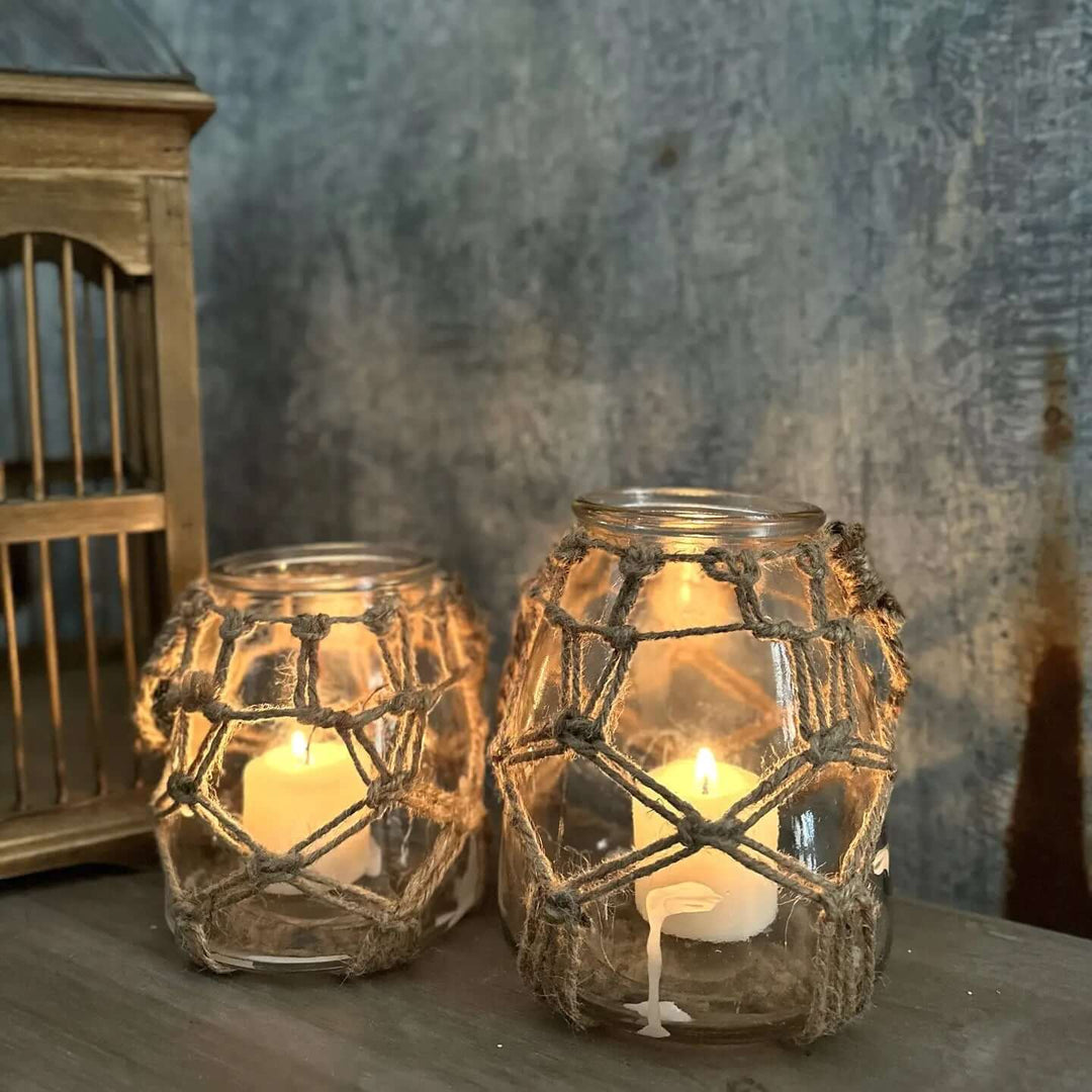 Small and medium rope-net glass vessels glowing with candles