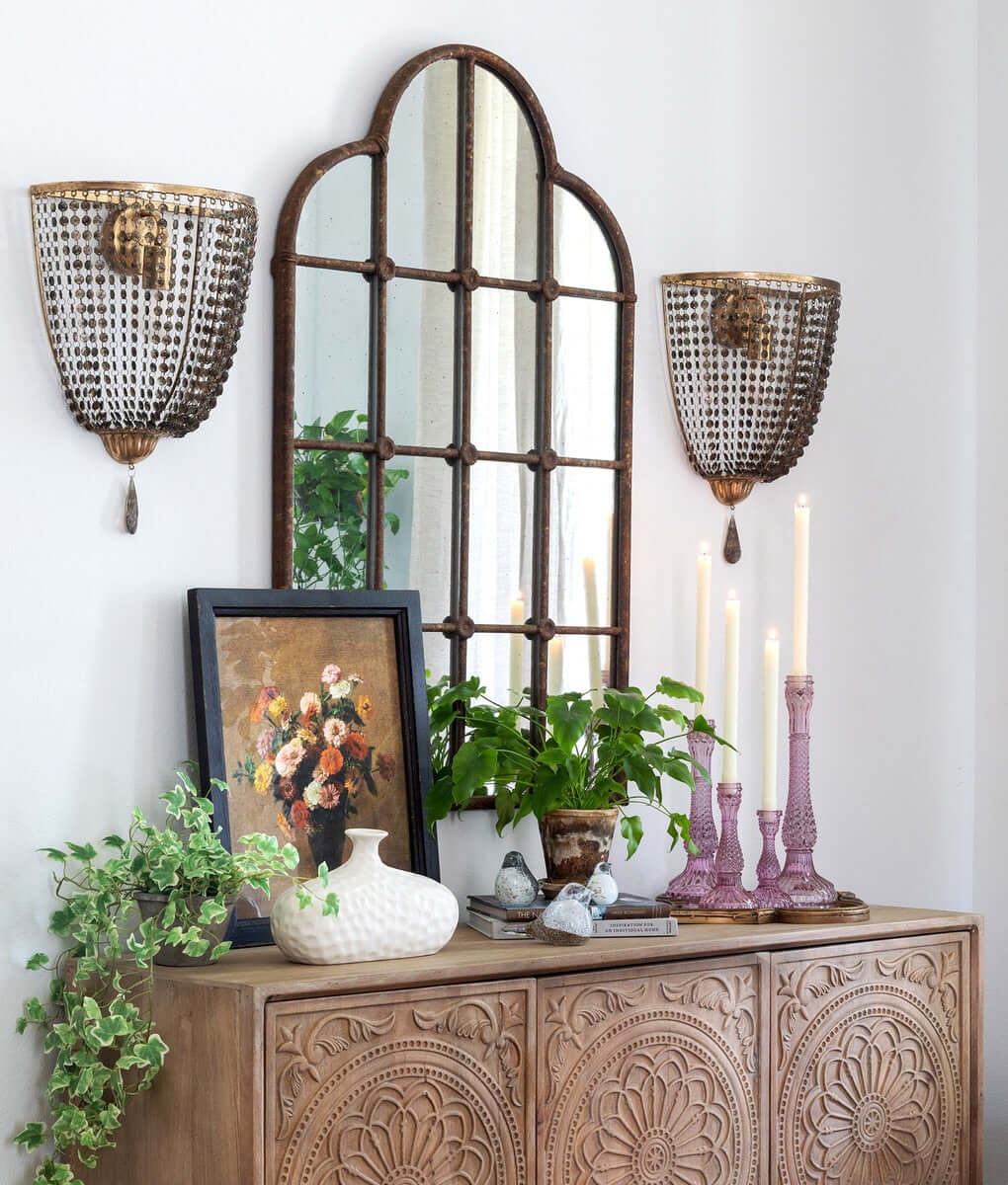 Rustic farmhouse iron windowpane mirror with vintage decor on wooden cabinet and wall-mounted lanterns.