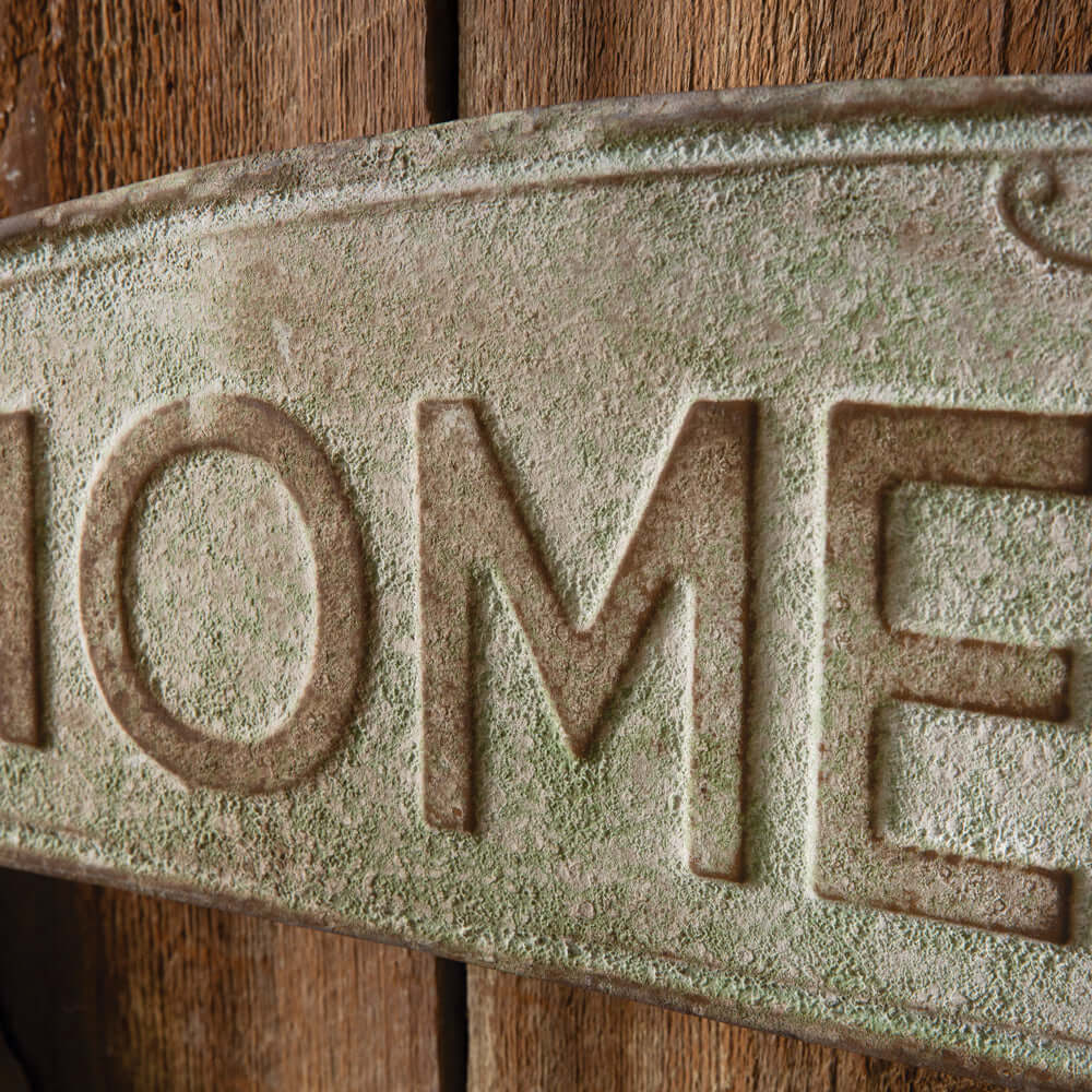 Close-up of rustic metal 'Homegrown' wall sign with a weathered green finish, reminiscent of vintage farm decor above a wooden background.