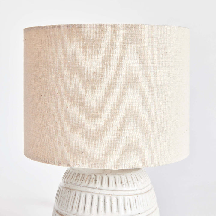 Close-up of a rustic textured pottery table lamp with a white glaze and natural linen shade.